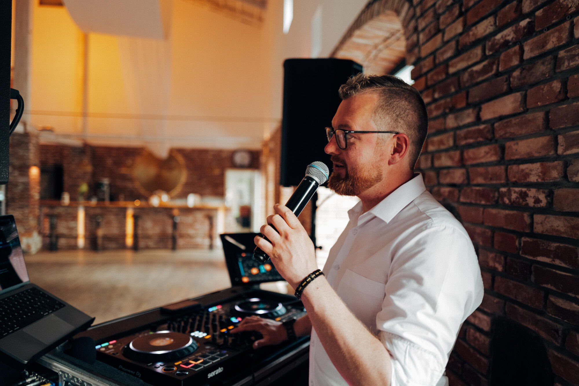 Dennis Genske moderiert mit Mikrofon am DJ-Pult